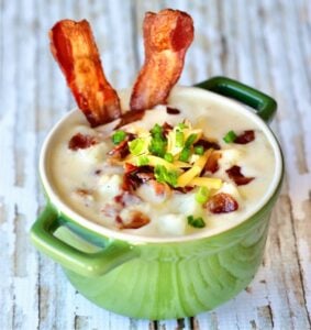 Loaded baked potato soup in bowl topped with bacon, shredded cheddar cheese and green onions.