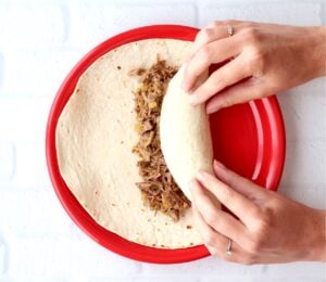 Beef burrito being rolled up in tortilla.
