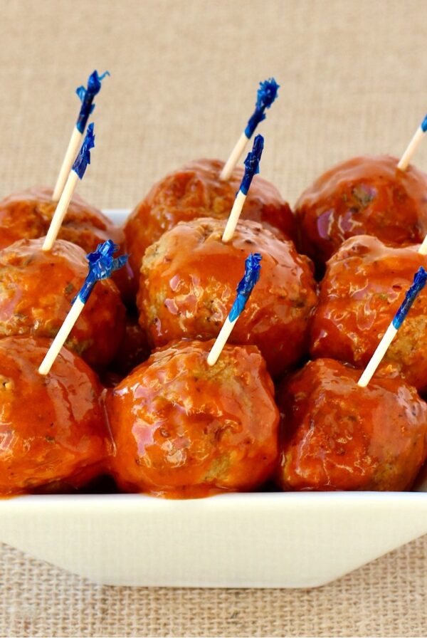 Buffalo wing meatballs in small dish with buffalo sauce on top and toothpicks inserted.