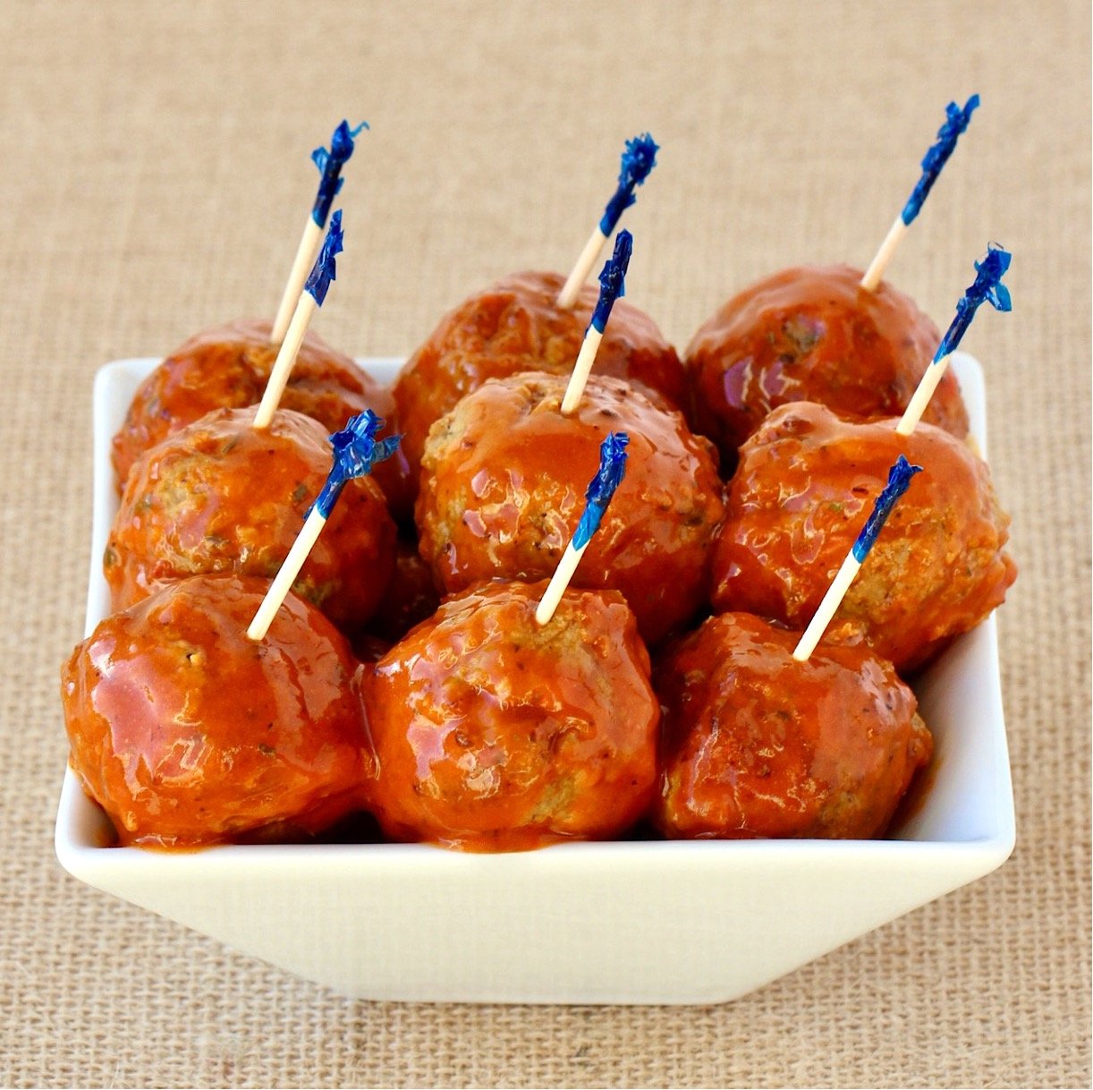 Buffalo wing meatballs in small dish with buffalo sauce on top and toothpicks inserted.