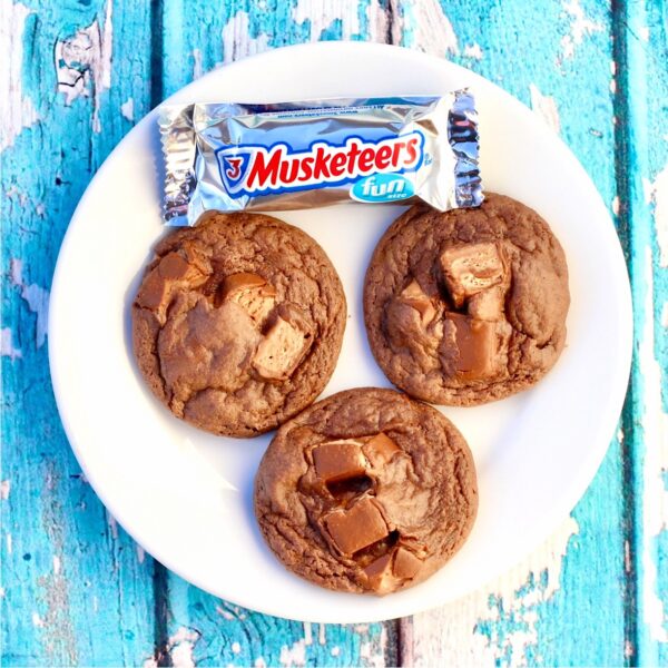 Three chocolate candy bar cookies on plate with 3 musketeers bar to the side.