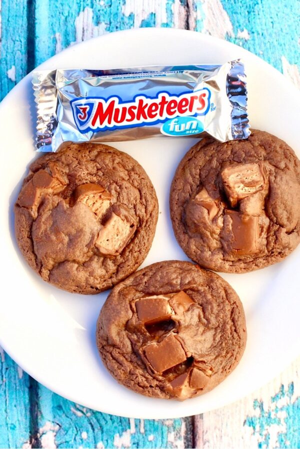 Three chocolate candy bar cookies on plate with 3 musketeers bar to the side.