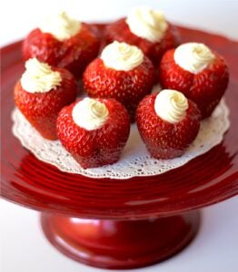 Seven cheesecake stuffed strawberries on cake plate.