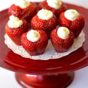 Seven cheesecake stuffed strawberries on cake plate.