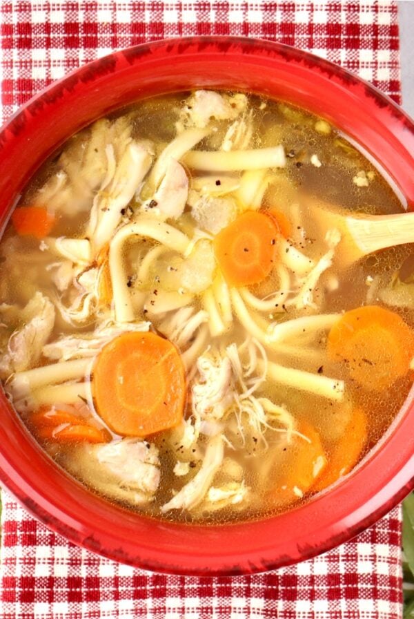 Chicken noodle soup in with carrots and rotisserie chicken in bowl.
