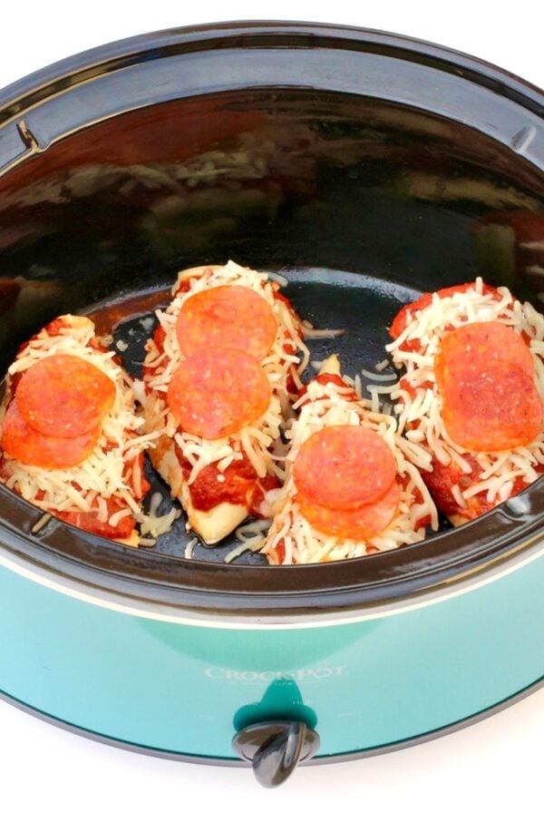 Four pieces of chicken in crockpot topped with pizza sauce, mozzarella cheese, and pepperoni slices.