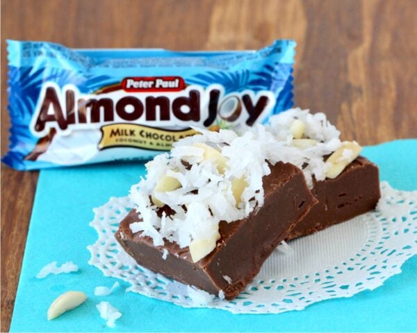 Two pieces of chocolate coconut fudge on doily with almond joy candy bar in background.