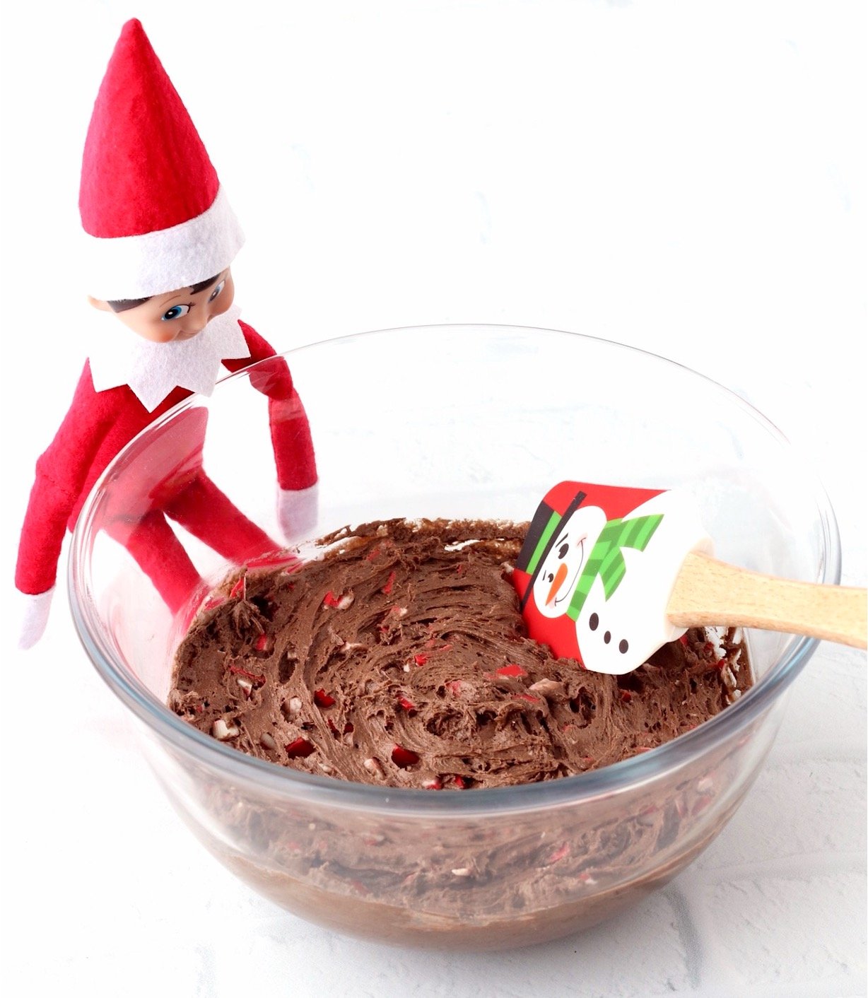 Christmas peppermint cookie dough in bowl with spatula and elf in the background.