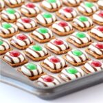 Christmas pretzel treats with Hershey's hugs and M&M's on cookie sheet.