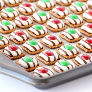 Christmas pretzel treats with Hershey's hugs and M&M's on cookie sheet.