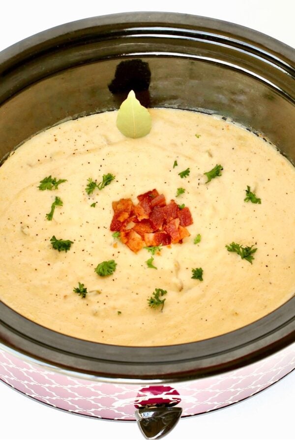 Crab chowder in crockpot garnished with bacon, parsley, and bay leaf.
