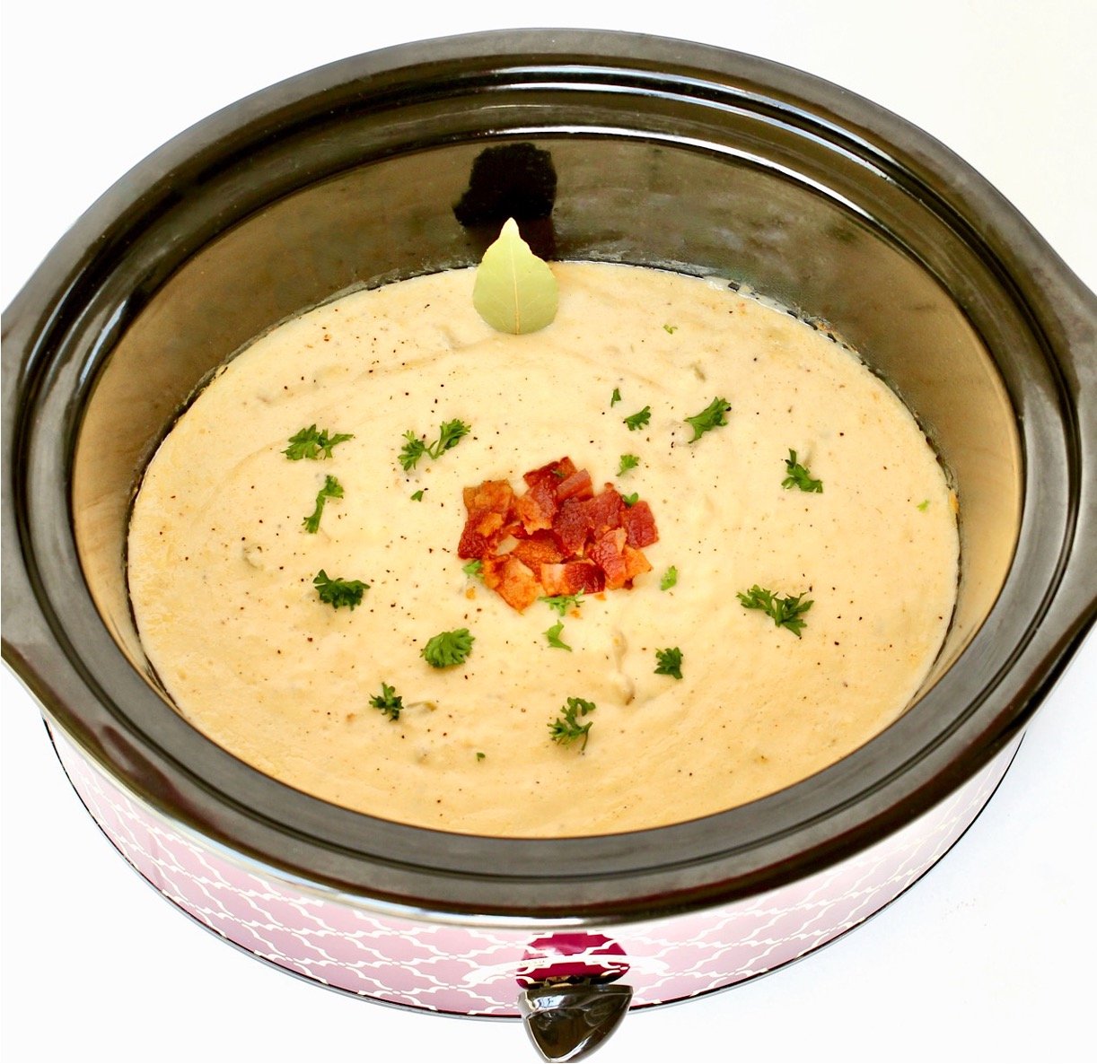 Crab chowder in crockpot garnished with bacon, parsley, and bay leaf.