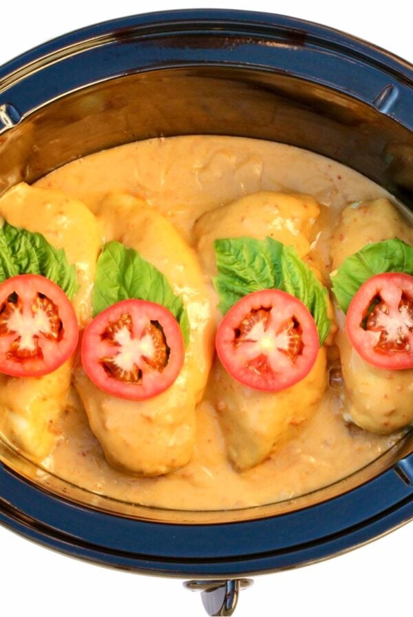 Creamy tomato chicken in crockpot with sauce, basil leaves, and tomato slices on top.