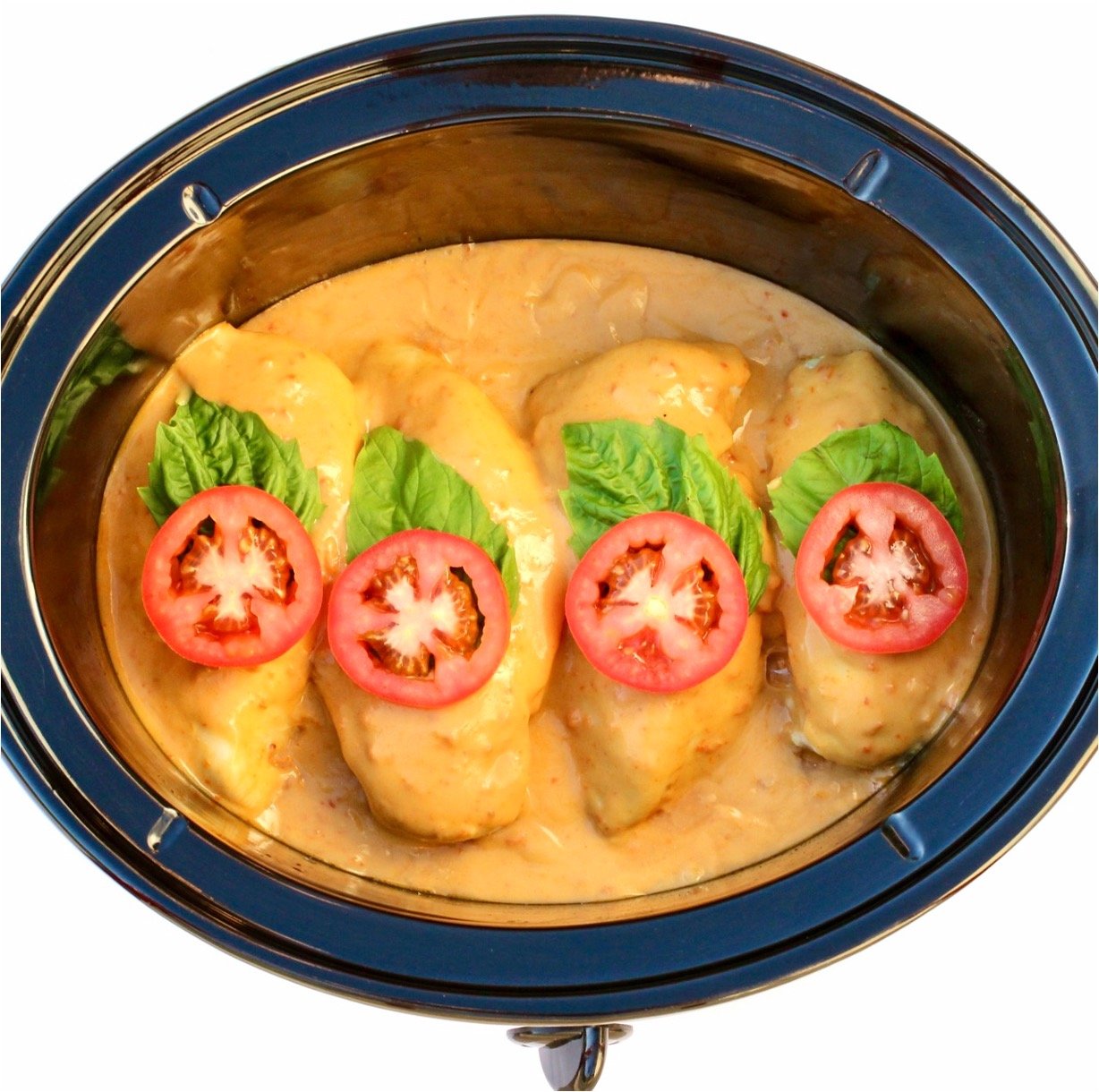 Creamy tomato chicken in crockpot with sauce, basil leaves, and tomato slices on top.