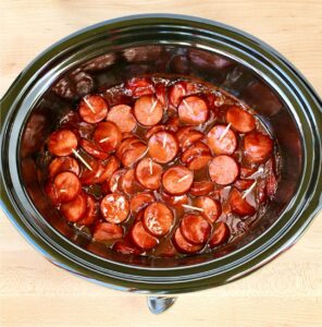 Kielbasa bites in crock pot with ranch seasoning and barbecue sauce, and toothpicks inserted.
