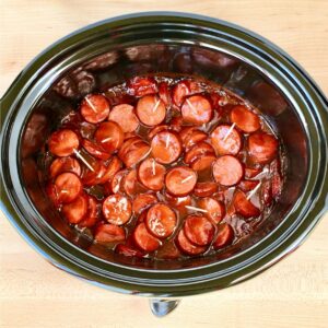 Kielbasa bites in crock pot with ranch seasoning and barbecue sauce, and toothpicks inserted.