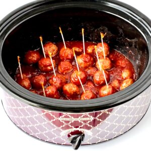 Meatballs with cranberry and chili sauce in crockpot with toothpicks inserted.