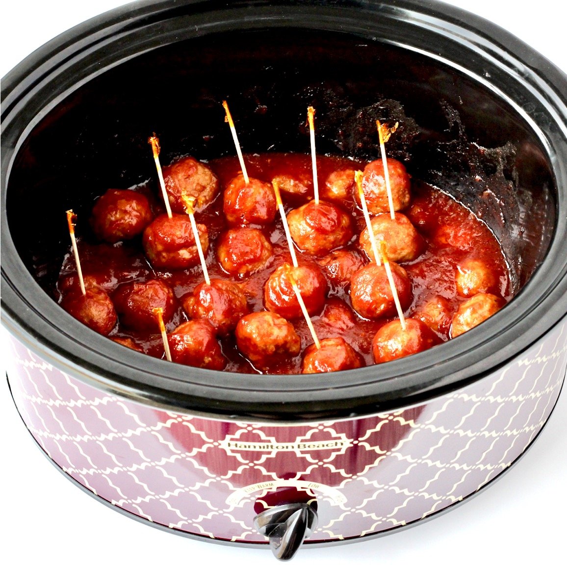 Meatballs with cranberry and chili sauce in crockpot with toothpicks inserted.