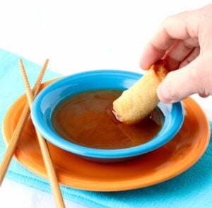 Sweet and sour sauce in bowl with egg roll being dipped in it.