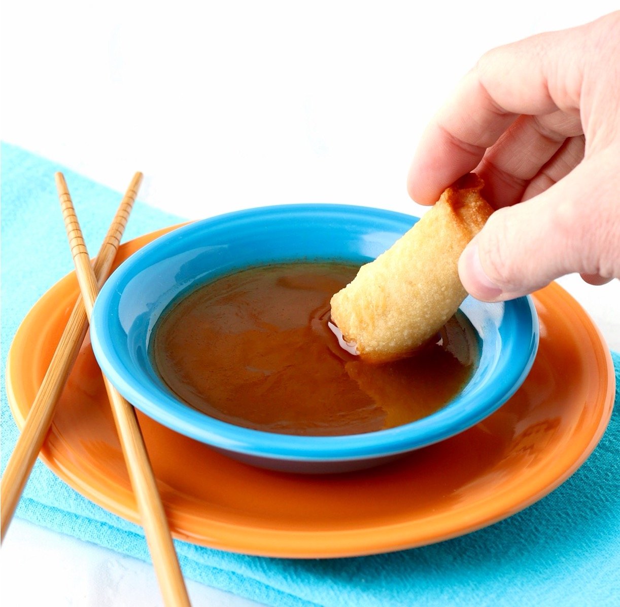 Sweet and sour sauce in bowl with egg roll being dipped in it.