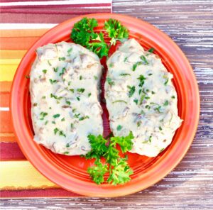Two pork chops smothered in French onion sauce on plate, garnished with fresh parsley.