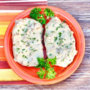 Two pork chops smothered in French onion sauce on plate, garnished with fresh parsley.