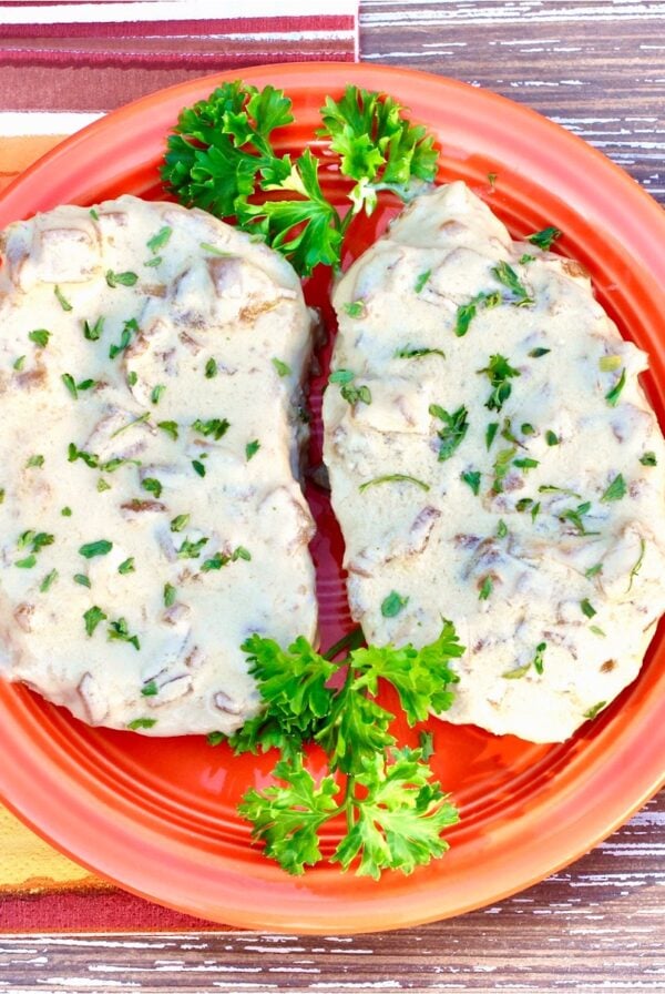Two pork chops smothered in French onion sauce on plate, garnished with fresh parsley.