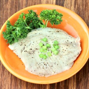 Grilled tilapia on plate with green onions on top and parsley to the side.