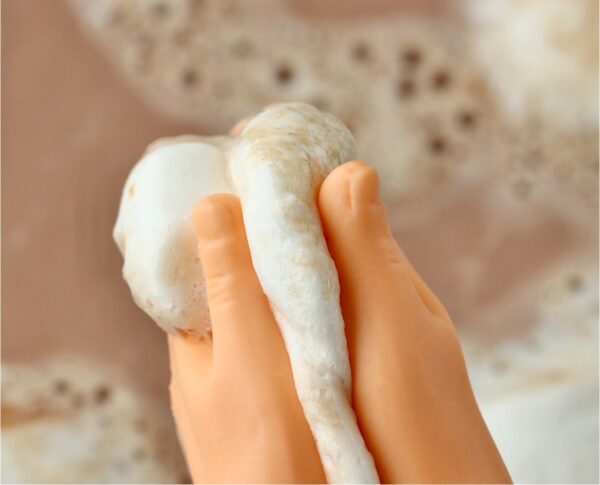 Tiny hands squishing marshmallow by crockpot filled with hot chocolate.