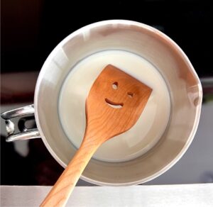 Milk for Peppermint Mocha warming on stove with smiling wooden spoon.