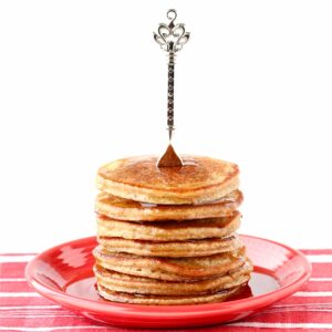 Stack of banana oat flour pancakes on plate, drizzled with syrup, and fork on top of stack.