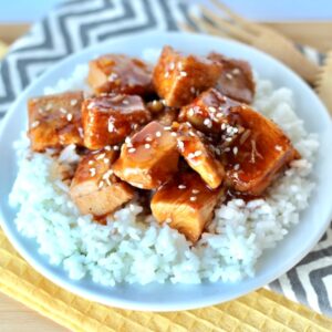 Cubed orange chicken on plate with rice, garnished with sesame seeds.