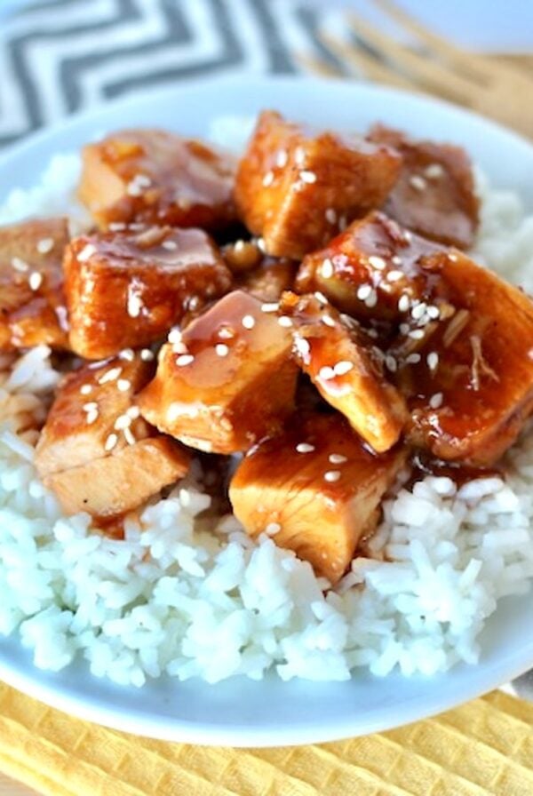Cubed orange chicken on plate with rice, garnished with sesame seeds.