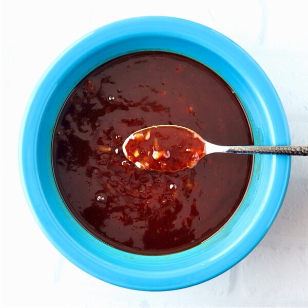Orange chicken sauce in bowl with spoon.