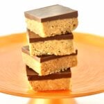 Stack of four chocolate peanut butter bars on orange cake stand.