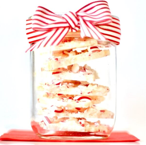 White chocolate peppermint bark pieces stacked in mason jar with bow.