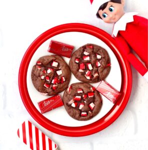 Three chocolate peppermint cookies on plate with elf and spatula to the side.