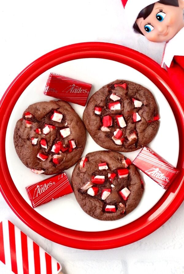 Three chocolate peppermint cookies on plate with elf and spatula to the side.
