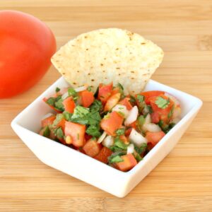 Pico de Gallo salsa with fresh tomatoes, onions, and cilantro in dish with tortilla chip.