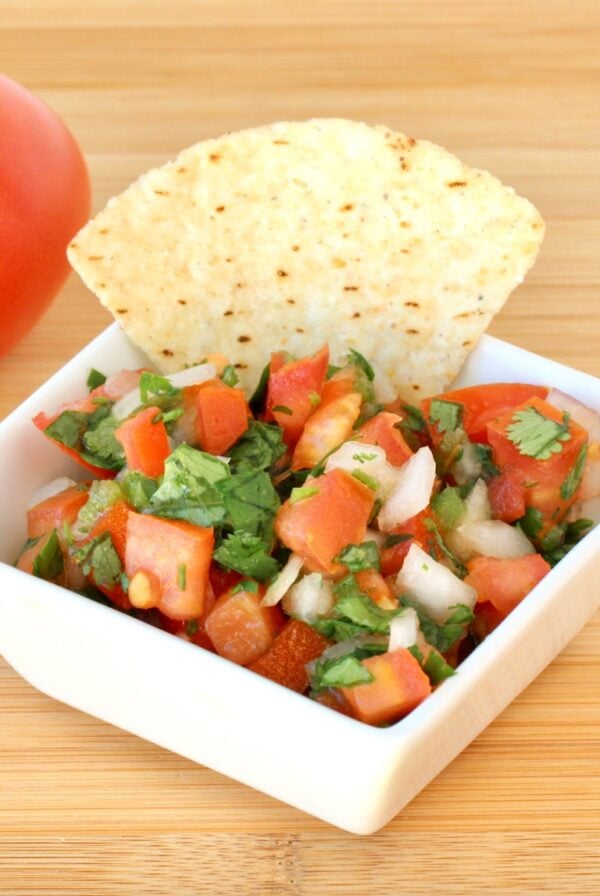 Pico de Gallo salsa with fresh tomatoes, onions, and cilantro in dish with tortilla chip.