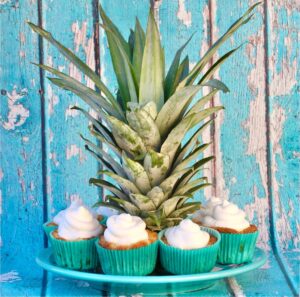Crown of pineapple on plate surrounded by pineapple cupcakes topped with cool whip.