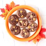 Seven salted caramel chocolate cookies on plate with leaves to the side.