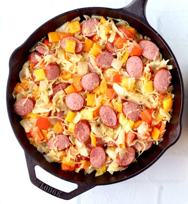 Kielbasa sausage and bell peppers with onion and sauerkraut in skillet.