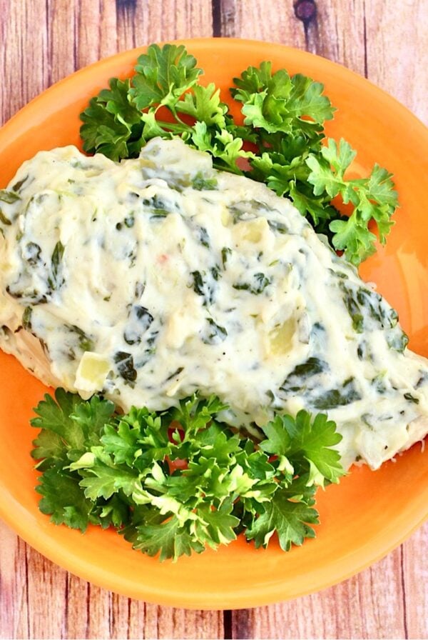 Piece of chicken on plate topped with creamy spinach artichoke sauce.