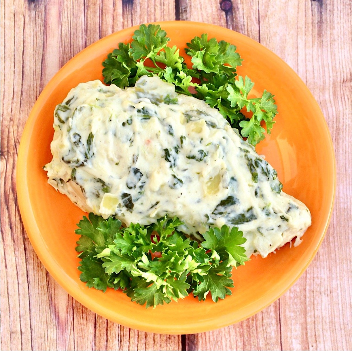 Piece of chicken on plate topped with creamy spinach artichoke sauce.