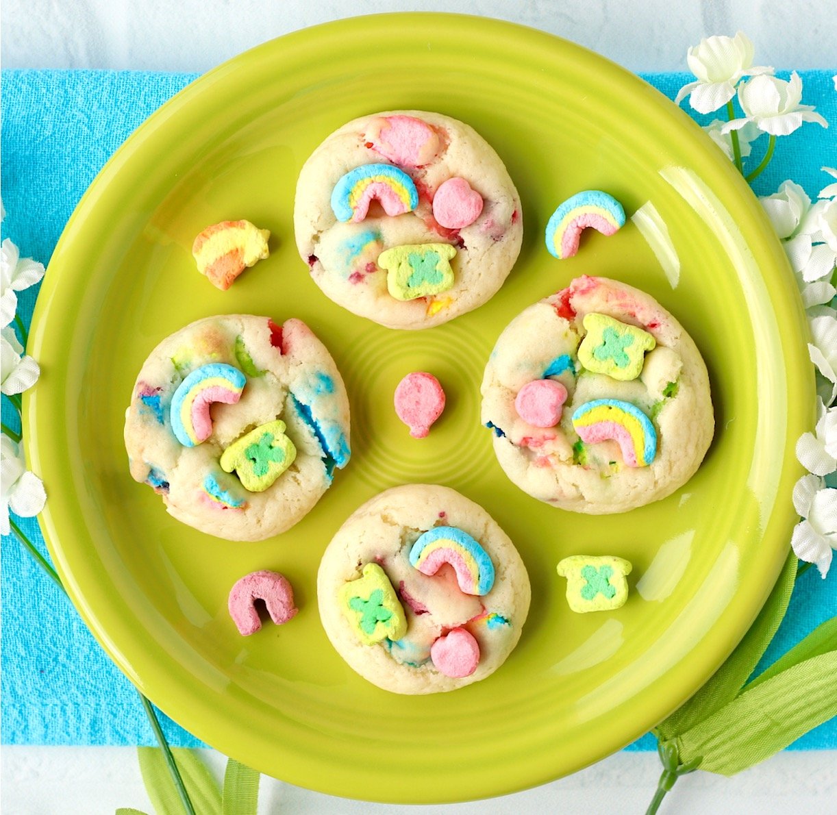 Four St. Patrick's Day cookies with Lucky Charms marshmallows on plate.