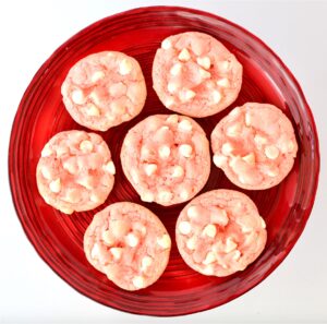 Seven pink strawberry white chocolate chip cookies on red plate.