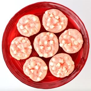 Seven pink strawberry white chocolate chip cookies on red plate.