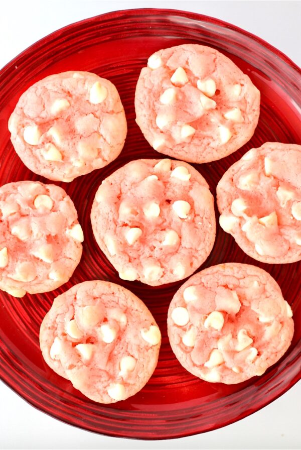 Seven pink strawberry white chocolate chip cookies on red plate.