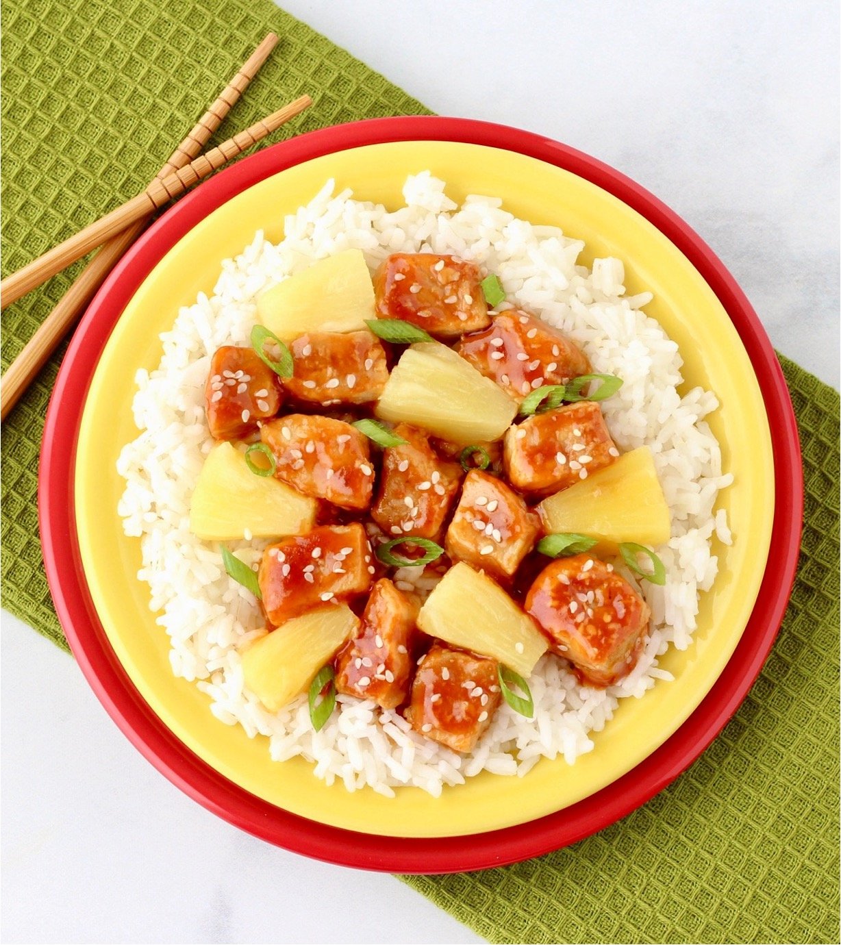 Sweet and sour pork with pineapples, green onions and sesame seeds on plate with rice.